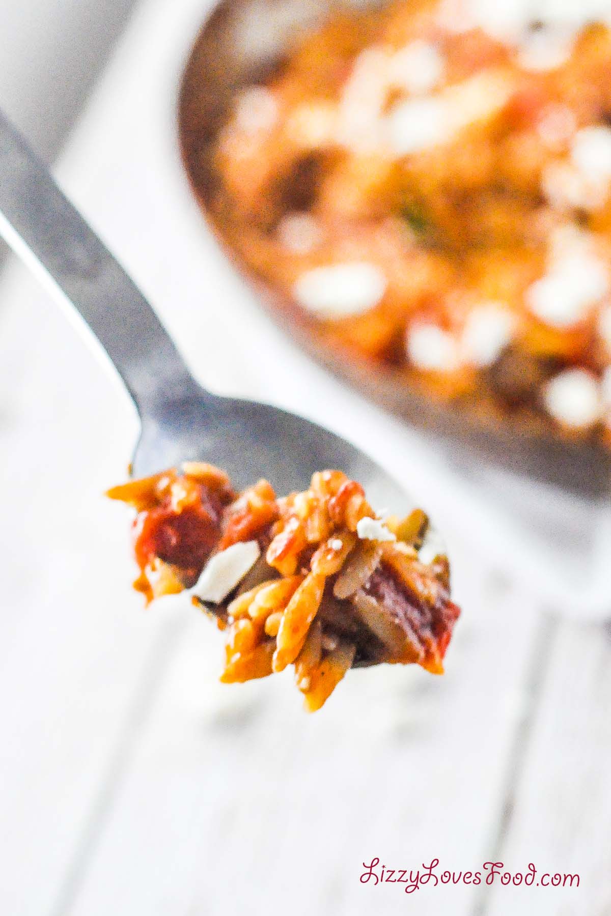 spoon full of Manestra Creamy Tomato Orzo in a pan on the table